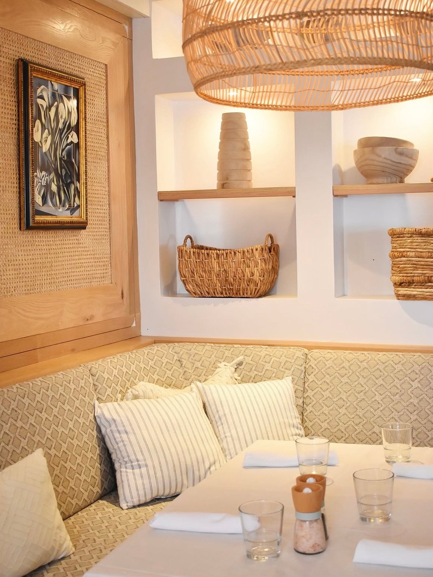 This cozy dining enclave radiates a serene Mediterranean warmth, blending artisanal textures like cane and rattan with soft, upholstered banquettes for an effortlessly chic feel. It is a masterclass in organic modernism, where curated earthy accents create a sanctuary-like atmosphere for intimate conversation.