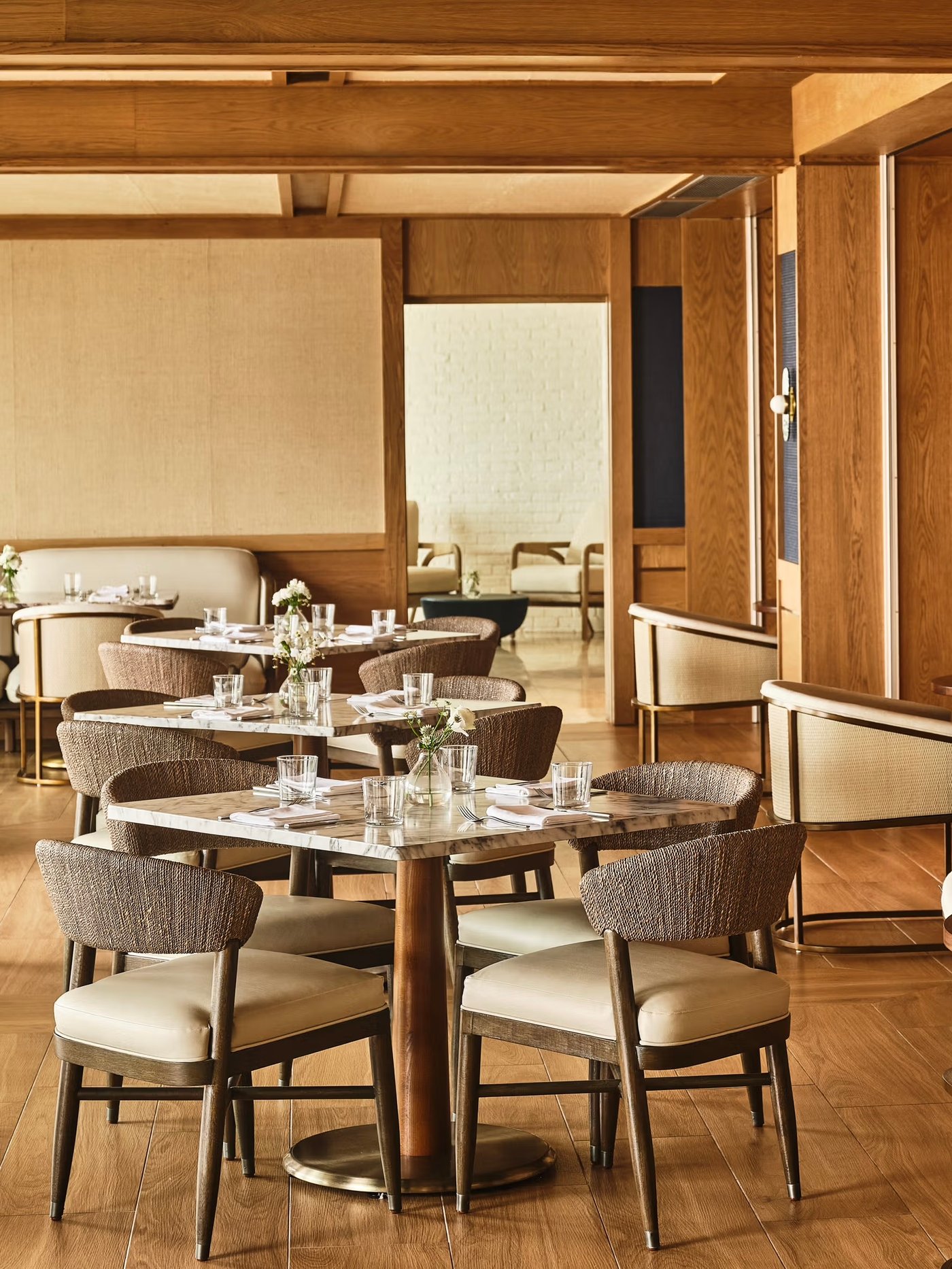 A masterclass in organic modernism, this dining space hums with a serene energy thanks to its golden wood tones and tactile woven textures. Every detail, from the veined marble tabletops to the soft linen accents, invites guests to linger over a long, sun-drenched lunch.