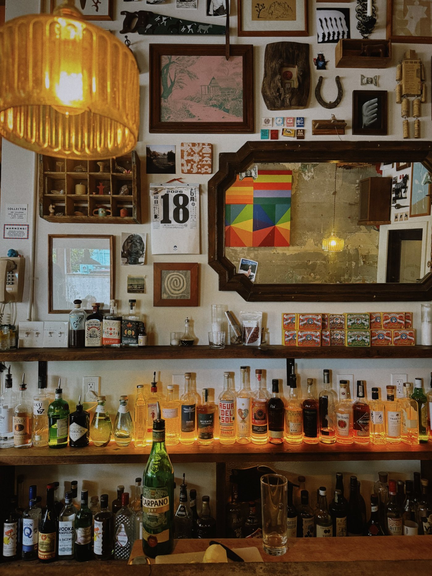 An impeccably curated maximalist bar that feels like a shared secret, blending nostalgic ephemera with a warm, amber-hued glow. The rhythmic organization of spirited bottles and vintage curiosities creates an atmosphere that is both intellectual and deeply inviting.