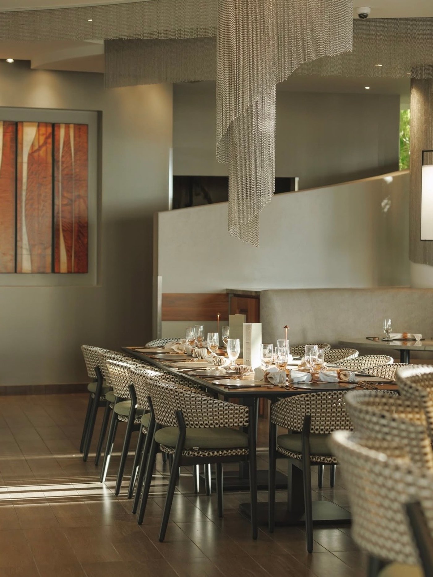 An exercise in understated luxury, this dining space marries organic textures with shimmering architectural details, bathed in a soft, late-afternoon glow. The dramatic beaded installation creates a sense of movement and height, perfectly complementing the tactile warmth of the woven seating.