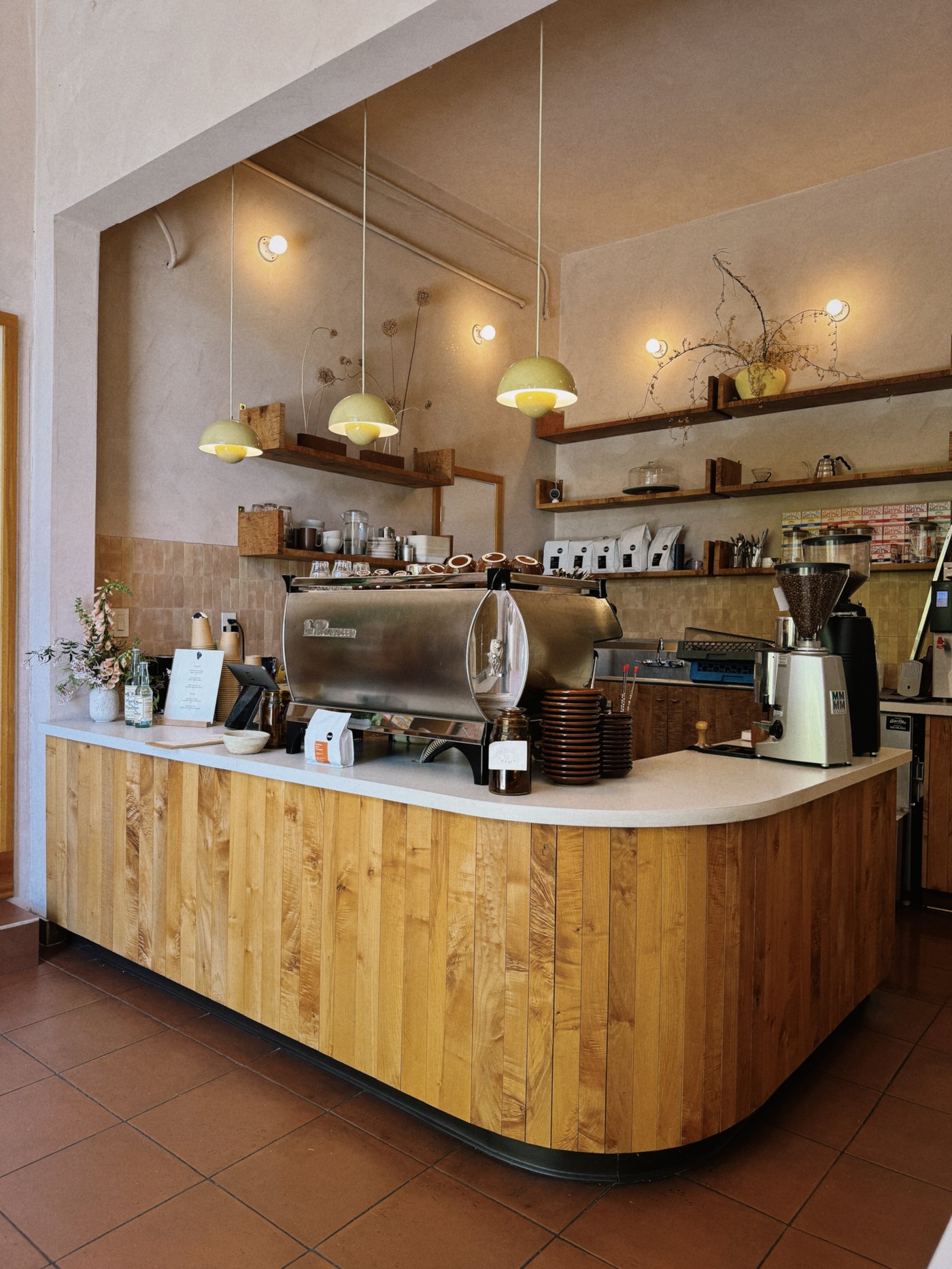 A masterclass in organic texture, this coffee bar blends warm wood slatting with mid-century lighting to create an inviting, tactile sanctuary for the caffeine connoisseur. The space feels grounded and artisanal, anchored by a soft palette that celebrates the beauty of natural materials.