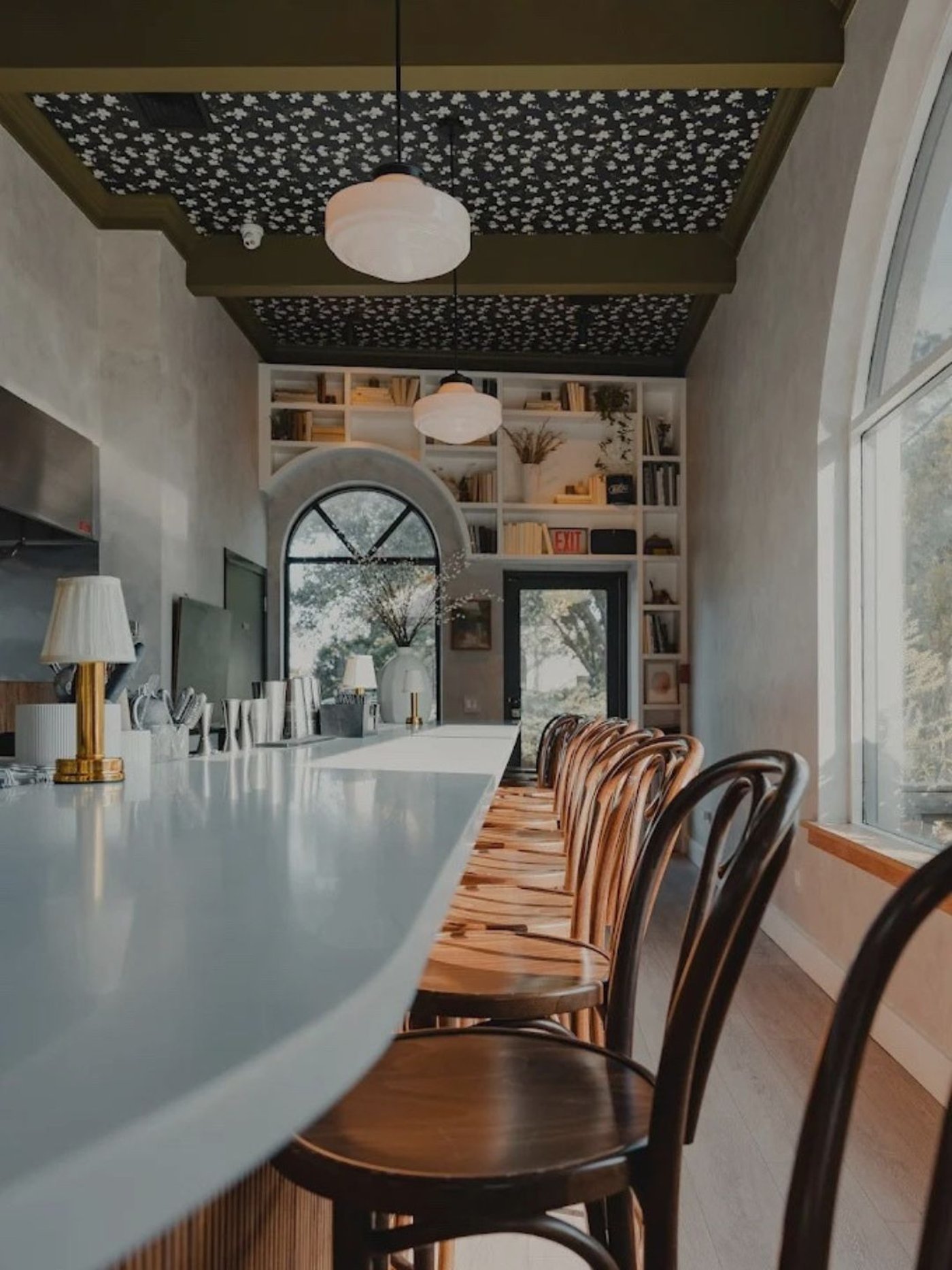 An intimate and intellectual drinking den that balances classical arched architecture with a whimsical floral-clad ceiling. The rhythmic warmth of bentwood stools against a pristine white counter creates a space that feels both nostalgic and modern.