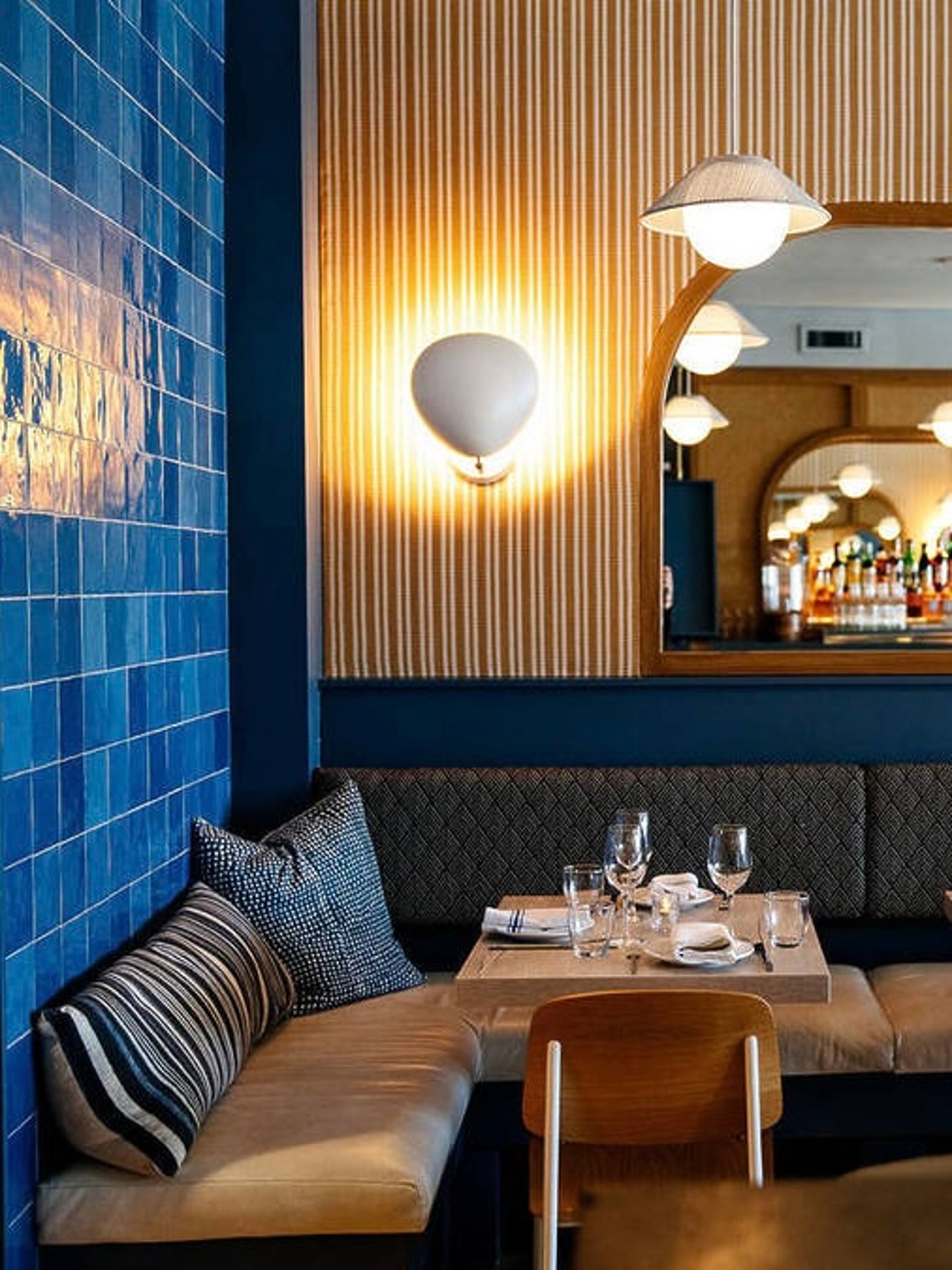 A masterclass in texture, this intimate dining corner blends glossy azure tiling with soft linens and glowing milk-glass lighting. The thoughtful layering of stripes and patterns creates a space that feels both meticulously curated and invitingly cozy.