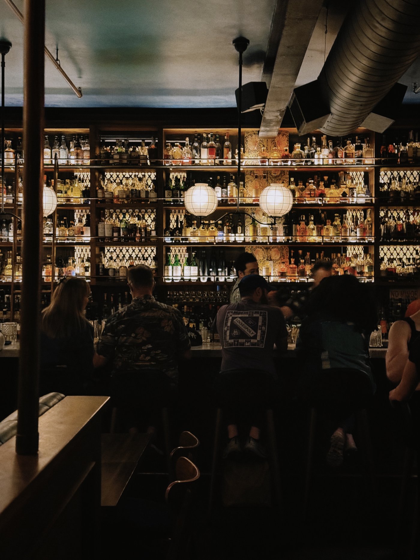 An intoxicating blend of industrial bones and gilded glamour, this bar features floor-to-ceiling backlighting that transforms spirits into a glowing library of liquid art. The soft radiance of globe pendants creates an intimate, low-lit sanctuary perfect for late-night secrets and perfectly stirred drinks.