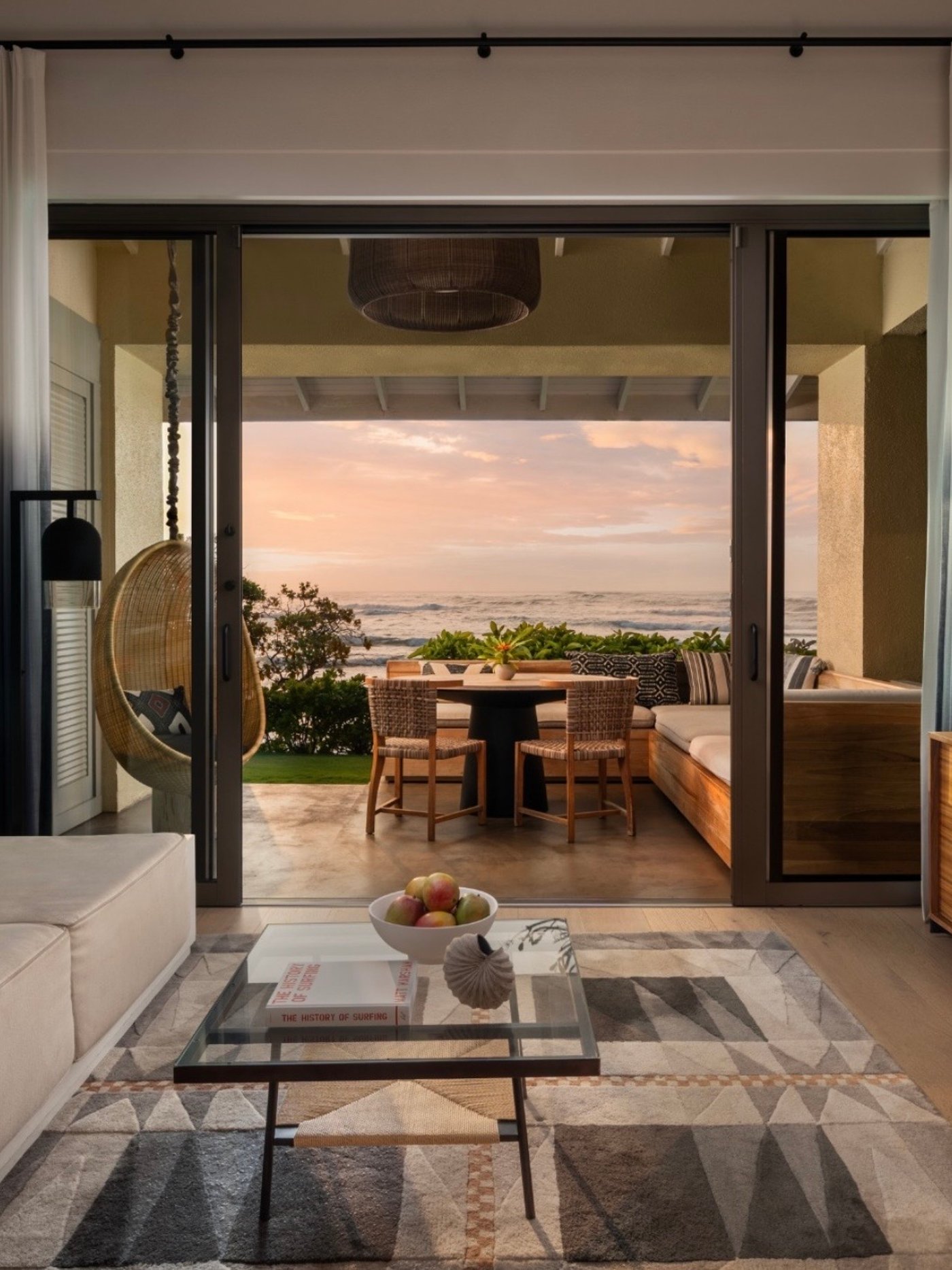 This serene coastal sanctuary perfectly blurs the line between high-end interior comfort and the raw beauty of the Pacific shoreline. Bathed in the soft, ethereal light of dusk, the space invites moments of quiet contemplation from the comfort of a hanging wicker nest or a sunset-facing banquette.