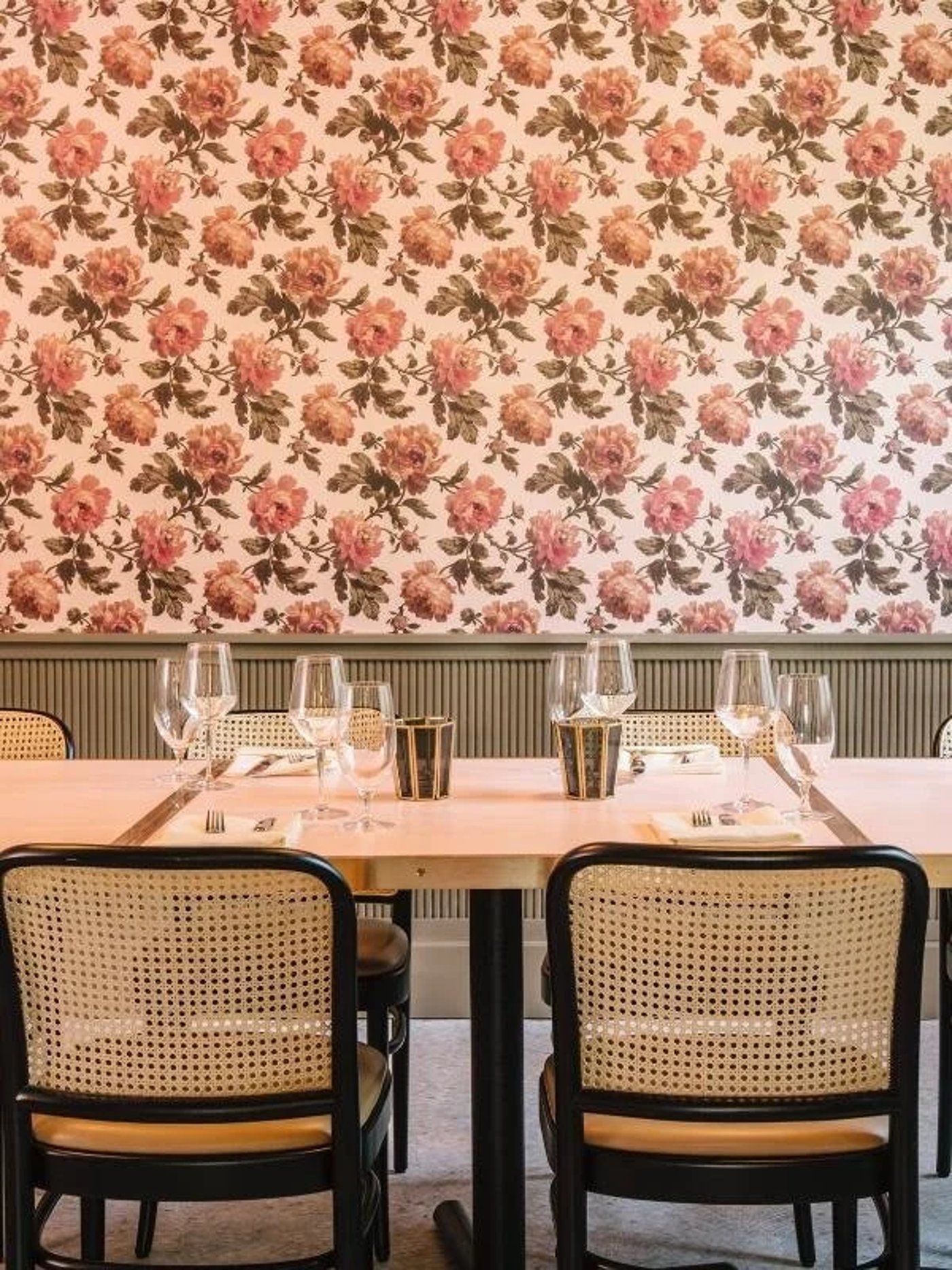 Blending lush botanical maximalism with mid-century textures, this dining nook feels like a secret garden reimagined for the modern host. The soft juxtaposition of pastel florals against structured cane seating creates an environment that is both nostalgically romantic and effortlessly cool.
