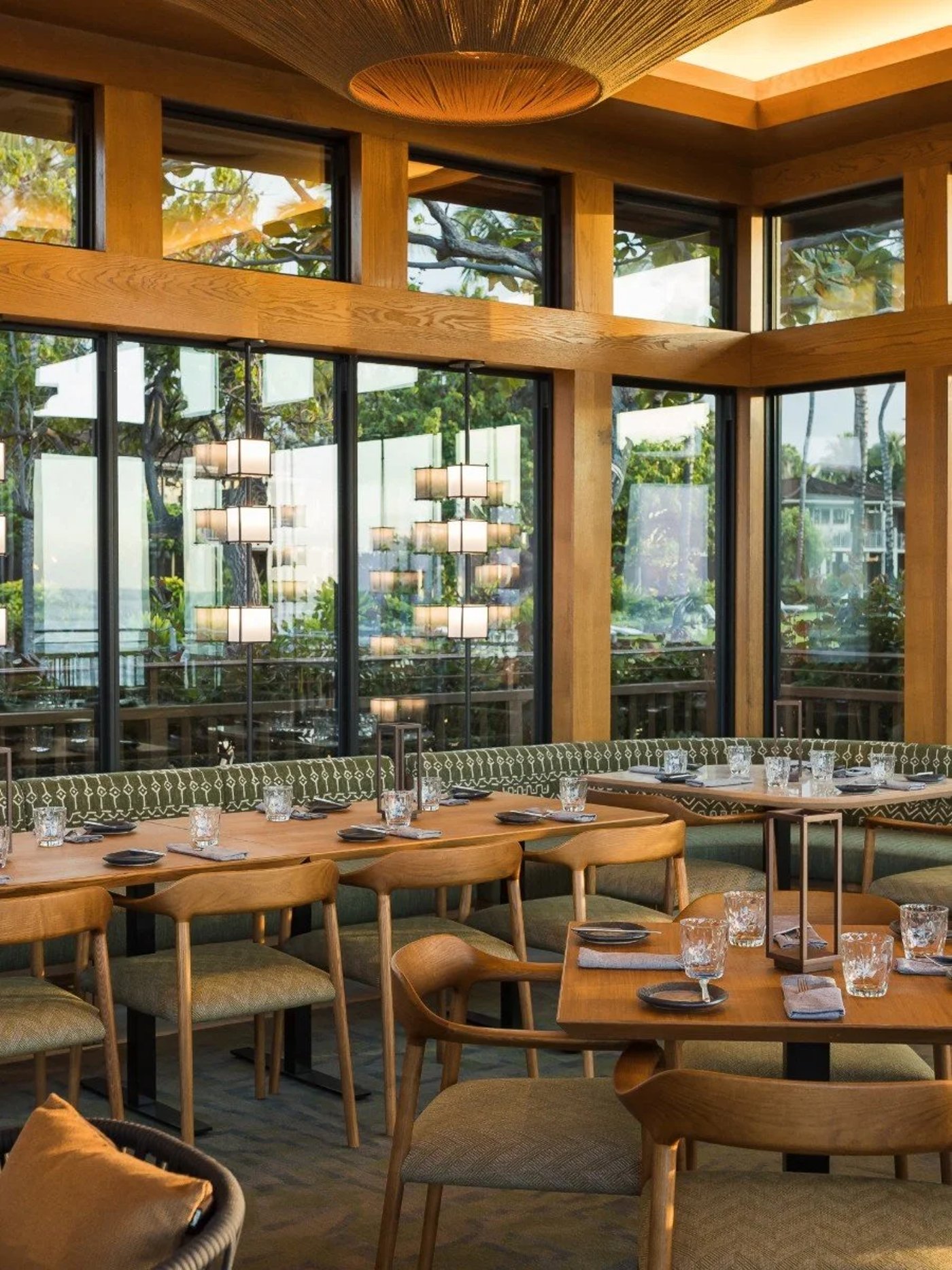 An inviting intersection of organic warmth and refined design, this sun-drenched dining space uses honey-hued timber and floor-to-ceiling windows to invite the lush surrounding foliage inside. The effortless blend of mid-century silhouettes and textured textiles creates a sophisticated yet relaxed atmosphere perfect for a lingering coastal meal.